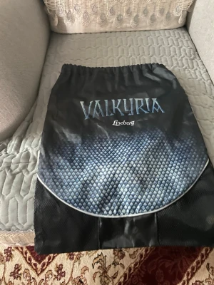 Svart gympåse Valkyria Liseberg - Säljer en svart gympåse med Valkyria-tryck från Liseberg. Väskan har snörning upptill och ett coolt blått mönster framtill som liknar fjäll. Praktisk dragkedja på baksidan för extra förvaring. Perfekt för att bära träningskläder eller småsaker. Finns i Göteborg att hämta 