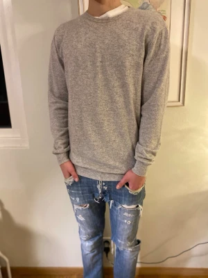 Grå cashmere tröja John Henric - Mjuk och stilren grå tröja från John Henric i lyxig cashmere. Perfekt för dig som gillar enkel och clean look. Passar dig som vill ha en skön och snygg tröja till hösten och vintern. Killen på bilden är 182cm | 70 kg, då storlek är L passar den någon lite större. Tröjan har ett mycket litet hål på bröstet som är lätt att åtgärda om man skulle villja och därav priset. Annars är den mycket bra skick.