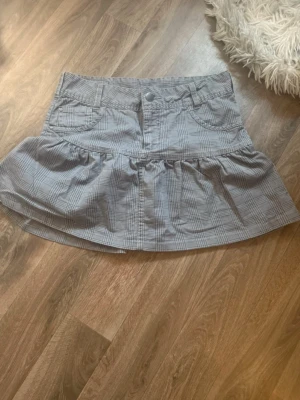 Grå rutig volangkjol i bomull Str S - Säljer en grå kortkjol med rutigt mönster och volangdetalj nedtill. Kjolen har fickor både fram och bak och är super söt 💕