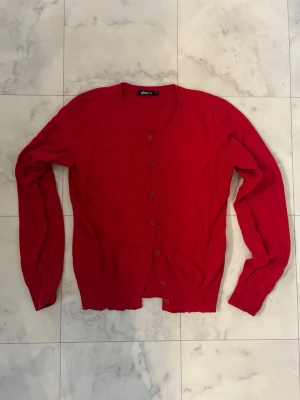 Röd kofta från Gina Tricot, M - Snygg röd kofta från Gina Tricot i storlek M. Koftan har rund halsringning, långa ärmar och knappar framtill. Perfekt att slänga över en t-shirt eller linne för en chill look. Materialet känns mjukt och lätt, troligen bomull eller syntet.