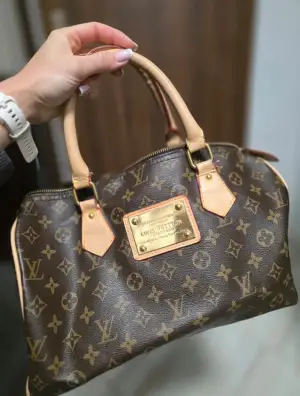 Säljer en klassisk handväska i brunt skinn med ikoniskt monogrammönster och detaljer i beige. Väskan har guldfärgade metalldetaljer, två handtag och dragkedja upptill. Insidan är svart med en innerficka med dragkedja. Fått som gåva och vet ej hur äkta den är, därav priset!🩷