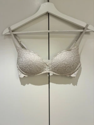 Beige bh från Intimissimi - Snygg beige bh från Intimissimi med vacker spets och dekorativ rosett framtill. Västen har justerbara axelband och ett elegant mönster i spetsen som ger en lyxig känsla. Använd lite.