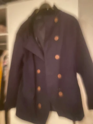 Rock av modell skäppar rock av hög kvalitet  - Säljer en stilren mörkblå skepparkavaj med dubbla rader guldiga knappar framtill. Jackan har klassisk krage och lång ärm, perfekt för dig som vill ha en snygg och tidlös look. Materialet känns robust och passar bra till höst och vinter.