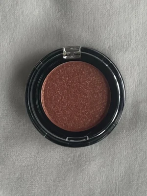NYX Utopia Rose Gold pigment - Säljer ett kompakt pigment från NYX i färgen Utopia Rose Gold. Färgen är en skimrande roséguld-ton som ger ett snyggt glow. Kommer i en rund svart dosa med transparent lock. Perfekt för att skapa kreativa looks med metallic finish.