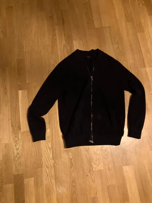 Marinblå kofta från Massimo Dutti - Snygg marinblå kofta från Massimo Dutti med hel dragkedja framtill. Tröjan är stickad i mjukt material och har ribbade muddar vid hals, ärmslut och nederkant. Perfekt för dig som gillar stilrena och klassiska plagg med modern touch.