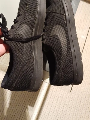 Svarta Nike sneakers mesh 43 - Svarta Nike sneakers med mesh-överdel och platt sula. Snyggt ton-i-ton Swoosh på sidan och klassisk snörning. Skorna har en sportig vibe och är riktigt lätta på foten. Perfekt för dig som gillar stilrena och bekväma sneakers.