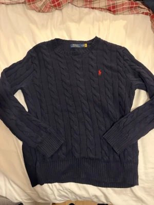 Mörkblå kabelstickad tröja Polo Ralph Lauren - Stickad premium-polo i fint skick med perfekt passform och lyxig kvalitet. Nypris ca 2200 kr. Säljs snabbt i det här skicket – köp innan någon annan tar den. ✅Beställ nu = Kommer innan Jul ✅Ställ frågor = Snabbt svar 