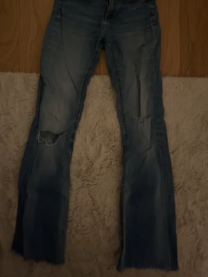 Blå jeans med slitna knän. Bootcut. Midwaist. - Säljer ett par blå jeans med slitningar och hål vid knäna. Dem är använda få gånger och är köpt från H&M. Bootcut!
