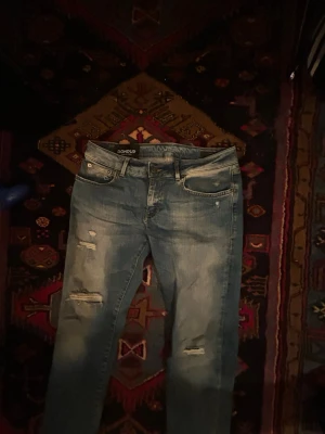 Blå jeans från Dondup - Snygga blå jeans från Dondup med slitningar och hål på benen för en trendig look. Klassisk femficksmodell med knapp och dragkedja. Jeansen har en ljus tvätt och är tillverkade i bomullsdenim. Perfekta för dig som gillar en avslappnad och cool stil. Är i modell Gaia, och har en relativt tight passform. Tagg medföljer ⭐️