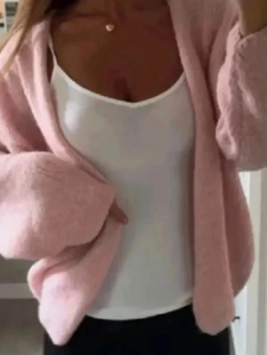 Ljusrosa stickad kofta från Lindex - Supermysig ljusrosa stickad kofta från Lindex med loose passform och långa ärmar. Koftan är öppen framtill utan knappar och har en fluffig, mjuk känsla. Perfekt att slänga över en topp för en chill look. Passar dig som gillar pastell och comfy vibes. Se defekt på sista bilden