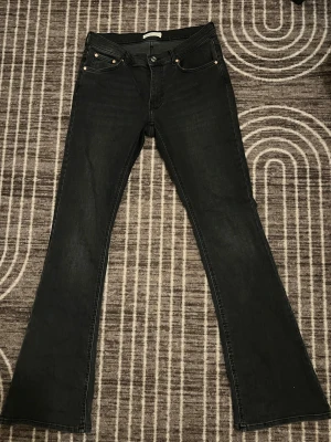Svarta bootcut jeans - Säljer ett par svarta jeans med bootcut passform. Klassisk femficksmodell med knapp och dragkedja framtill. Jeansen har en snygg mörk ton och är tillverkade i jeansmaterial med lite stretch för extra komfort.
