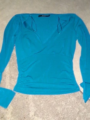 Turkos omlottopp från Bik Bok XS - Säljer en turkos omlottopp från Bik Bok i storlek XS. Toppen har långa ärmar, v-ringning . Materialet är mjukt och stretchigt, med rynkade detaljer i midjan för en snygg passform.