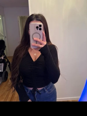 Svart ribbad långärmad topp med snörning - Svart långärmad topp från Funky Buddha med ribbad struktur och v-ringning. Toppen har snörning framtill som ger en snygg rynkad effekt och croppad passform. Perfekt att styla med jeans eller kjol för en trendig look.