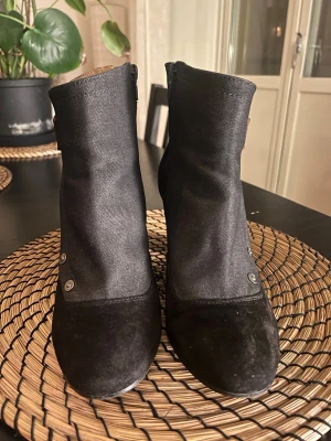 G-star Raw svarta stövletter med klack - Snyggas svarta stövletter från G- Star Raw med grov klack och rund tå. Skorna är tillverkade i mocka och jeans, har dekorativa metallknappar och ett brunt spänne på sidan. Dragkedja på insidan för enkel påtagning. Perfekt för dig som gillar stilrena och coola boots. #gstar #stövletter