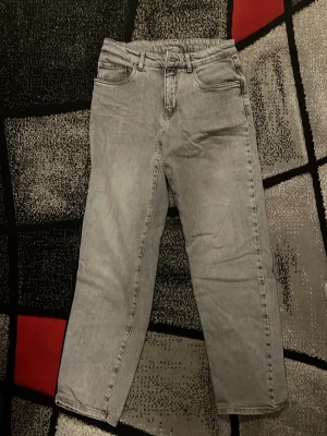 Grå jeans från Kappahl, rak modell - Säljer ett par grå jeans från Kappahl i rak modell. Jeansen har klassisk femficksdesign, bälteshällor och dragkedja med knapp. Snyggt tvättad denim som ger en cool vibe och passar till det mesta. Perfekt för dig som gillar enkel och stilren look.