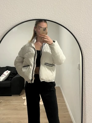 Vit pufferjacka med svarta detaljer - Säljer en vit pufferjacka med svarta detaljer vid dragkedja och fickor. Jackan har hög krage, två stora fickor framtill och stängs med dragkedja. Perfekt för kyliga dagar och ger en clean, modern vibe.