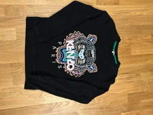 En lite tjockare tröja av märket kenzo  - En fin tröja i färgen svart med en stor kenzo detalj mitt på tröjan. Den har inga hål eller större anmärkningar men har använts måttligt. 