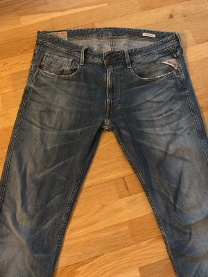 Replay Anbass jeans blå 34/34 - Säljer ett par Replay Anbass jeans i klassisk blå tvätt med snygga slitningar och broderade detaljer på bakfickorna. Modellen har normal passform och raka ben, med Replay-logga på fickan och patch bak i midjan. Perfekt för dig som gillar stilrena jeans med lite edge.