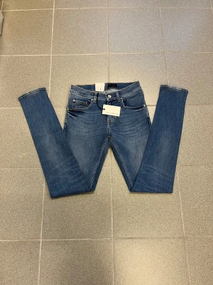 Blå slimmade jeans från Tiger of sweden W29 L34 - Snygga blå jeans från T/J med smal passform och smala ben. Klassisk femficksmodell med bruna sömmar och läderpatch bak i midjan. Jeansen är i stretchigt denim och har dragkedjegylf. 