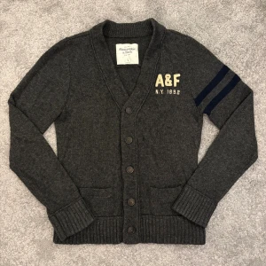 Abercrombie & Fitch Cardigan - Tja! Säljer nu denna riktigt schyssta mörkgråa cardiganen från Abercrombie & Fitch. Cardiganen är i bra skick och är storlek L, men skulle säga att den sitter mer åt M. 679kr, men kan såklart diskuteras.