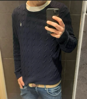 Mörkblå kabelstickad tröja Polo Ralph Lauren - Säljer en mörkblå kabelstickad tröja från Polo Ralph Lauren i storlek L. Tröjan har rund hals, diskret broderad logga på bröstet och är gjord i 100% bomull. Perfekt för dig som gillar klassisk och stilren look.