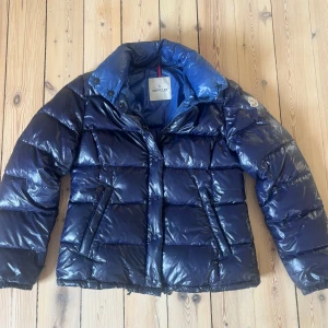 Pufferjacka från Moncler - Äkta Moncler jacka dam. Kod för äkthetsbevis finns i jackan. Jackan är i storlek 4 och passar xs-m. Färgen på jackan är blå/lila. 