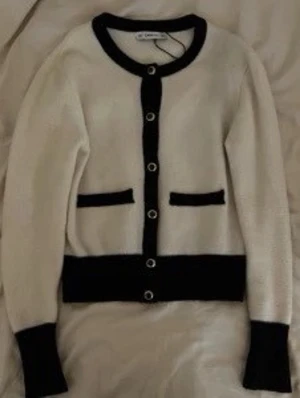 Beige och svart kofta med knappar - Snygg beige kofta från Copenhagen Muse med svarta detaljer vid krage, knäppning, fickor, ärmslut och nederkant. Klassisk rund halsringning och dekorativa knappar framtill. Perfekt för lager-på-lager och stilrena outfits.