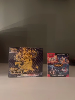 Pokémon Surging Sparks – ETB + Booster Bundle (Sealade & Oöppnade) - 1 st Surging Sparks Elite Trainer Box (ETB) – helt oöppnad & fabriks-sealad 1 st Surging Sparks Booster Bundle – oöppnad & fabriks-sealad  Paketeras mycket noggrant och skyddas väl vid frakt.