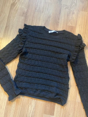 Svart stickad tröja med volanger från Zara - Svart stickad tröja från Zara i storlek M men passar som S. Tröjan har långärmade ärmar, volangdetaljer på axlarna och ett snyggt ribbat mönster över hela plagget. Har några lösa trådar som syns på bilden men annars fin!💕