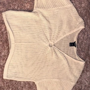 Beige stickad topp från Lindex XS - Säljer en beige stickad topp från Lindex i storlek XS. Toppen är ärmlös med en luftig, virkad känsla och har en snygg twist-detalj framtill. Perfekt för varma dagar och enkel att styla med jeans eller kjol.