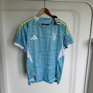 Juventus 25/26 matchtröja Adidas - Juventus fotbollströja från Adidas i ljusblått med abstrakt mönster, vita detaljer och gula ränder på axlarna. Kortärmad modell med rund hals och ventilerande meshpaneler på sidorna. Perfekt för dig som vill sticka ut på planen.