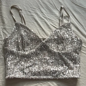 Glittrig silver paljettopp - Säljer en glittrig croppad topp i silver med tunna justerbara axelband. Hela toppen är täckt av paljetter som ger en riktigt festlig vibe. Materialet är polyester och toppen har en figurnära passform. Perfekt för dig som vill sticka ut och glänsa 🤍