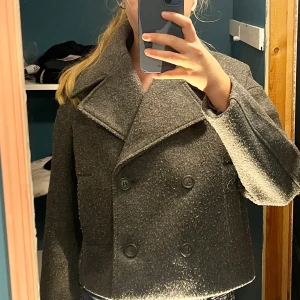 Grå kappa  - Säljer en grå kort kappa från lager 157 i storlek XS. Jackan har bred krage, dubbelknäppning med stora knappar. Säljer eftersom att den inte används. Två av knapparna har trillat av men de är påsydda igen. Nypris : 400 