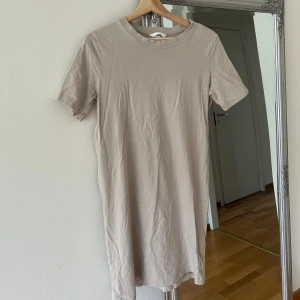 Beige t-shirtklänning i bomull - Enkel och stilren beige t-shirtklänning med rund halsringning. Klänningen är rak i modellen och gjord i mjuk bomull, perfekt för en avslappnad look. Knappt använd