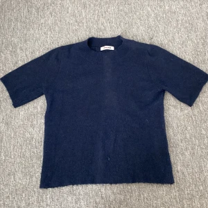 Mörkblå stickad tröja J'aime Olyto - Mörkblå stickad tröja från J'aime Olyto med korta ärmar och ribbad halsringning. Använd få gånger fortfarande i väldigt bra skick.