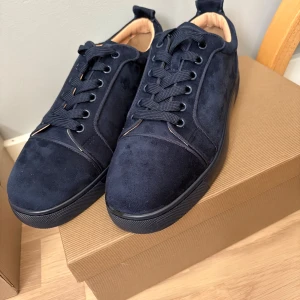 Mörkblå sneakers från Christian Louboutin - Snygga mörkblå sneakers från Christian Louboutin i mocka med klassisk röd sula och svarta snören. Skorna har rund tå och platt sula, samt exklusiva detaljer och branding på sulan. Perfekta för dig som vill sticka ut med stil. Storlek 40 men är stora i storleken. Pris kan diskuteras 