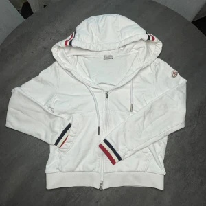 Vit Moncler zip-up - ‼️den har blivit för liten för mig💛 | Priset är ej skrivet i sten, både tjejer och killar passar i denna💛 var inte rädd för att ställa frågor💭 | Vit hoodie från Moncler med dragkedja framtill och huva med snörning. Tröjan har långa ärmar och ribbade muddar med röd, vit och blå rand. Moncler- på vänster ärm. Perfekt för dig som gillar stilrena och sportiga plagg.