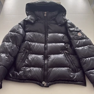 Svart Moncler pufferjacka med huva - Hej säljer nu min moncler maya för att dem blivit för liten. Den har ett väldigt litet hål i högra armbågen men annars så är den i bra skick. Storlek M
