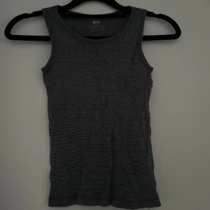 Grå linnetopp från H&M - Säljer en grå ribbad linnetopp från H&M i ekologisk bomull. Toppen är ärmlös med rund halsringning och har ett diskret, smalrandigt mönster. 