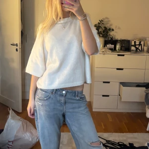 Vit stickad tröja - Säljer en vit croppad stickad tröja med breda, korta ärmar och rund hals. Tröjan har en avslappnad passform och är perfekt för lager-på-lager. Enkel och stilren design som passar till jeans eller kjol.