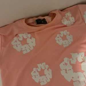 Denim tears rosa t shirt  - Säljer en rosa t-shirt från Denim tears med coola vita blommönster över hela tröjan. T-shirten har rund hals och korta ärmar, perfekt för dig som gillar färg och mönster. Materialet känns mjukt och skönt mot huden. Den är helt ny och priset kan diskuteras skriv gärna för frågor
