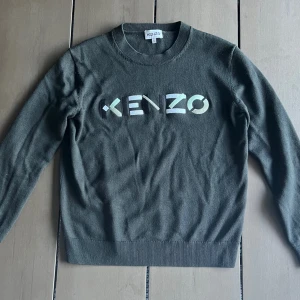 Mörkgrön stickad Kenzo tröja - Snygg mörkgrön stickad tröja från Kenzo med broderad logga på bröstet. Rund hals och ribbade muddar vid ärmslut och nederkant. Kan inte se att tröjan tillverkas längre, men liknande modeller med andra färger säljs för 283 dollar. 2678kr, mitt pris 649kr!