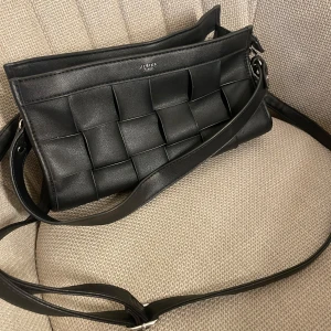 Handväska - Svart handväska från Ulrika Sweden. Ett kort avtagbart band och ett långt justerbart band tillkommer. Väskan har lite fläckar i innerfodret