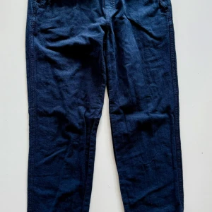 Mörkblå linnebyxor med rak passform - Snygga mörkblå linnebyxor med rak passform. Byxorna har klassisk design med fickor i sidorna och är perfekta för en avslappnad men stilren look. Materialet är lätt och andas, vilket gör dem sköna att bära under varmare dagar.