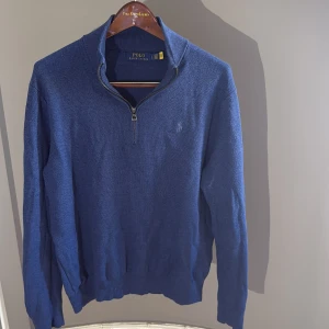 Blå half zip från Ralph Lauren - Snygg blå långärmad tröja från Polo Ralph Lauren med half zip-dragkedja och diskret broderad logga på bröstet. Tröjan har en klassisk passform och är tillverkad i mjukt bomullsmaterial, perfekt för lager-på-lager under kyliga dagar. Nypris 1800