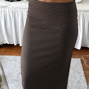 Rutig långkjol från Gina Tricot - Snygg långkjol från Gina Tricot i storlek S med klassiskt rutigt mönster i svart och beige. Kjolen har rak passform och är tillverkad i ett mjukt syntetmaterial som sitter bekvämt. Perfekt för dig som gillar stilrena och trendiga plagg. Med resårband i midjan! 