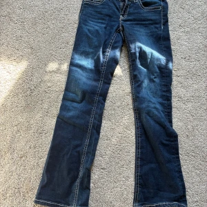 Blå bootcut jeans från Gina Tricot - Snygga blå jeans från Gina Tricot i bootcut-modell med markerade kontrastsömmar och coola fickdetaljer med lock och knapp både fram och bak. Jeansen har klassisk dragkedja och knapp framtill och är tillverkade i mjukt denimtyg.