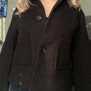 Svart ulljacka med stora knappar - Säljer en svart jacka i ull med stora knappar framtill och två rejäla fickor. Jackan är från Lager 157 och är i storlek S. Ordinarie pris är 400/350kr, men säljer den för 250kr. Perfekt nu till hösten. 