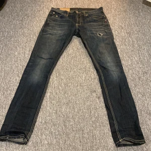 Mörkblå jeans från Dondup - Snygga mörkblå jeans från Dondup med slitningar och en trasig detalj på låret. Klassisk femficksmodell med kontrastsömmar och coola bakfickor med broderad detalj. Jeansen har normal passform och är tillverkade i jeansmaterial.