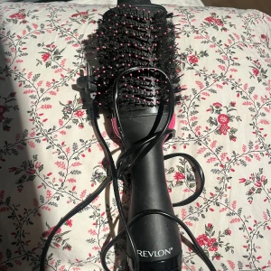Revlon One-Step Volumizer borste - Revlon One-Step Volumizer är en svart och rosa rundborste med borst och piggar, perfekt för att styla och torka håret samtidigt. Ergonomiskt handtag och sladd för enkel användning. Ger volym och glans till håret på nolltid.